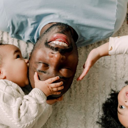 Two children playing with man lying on the floor
